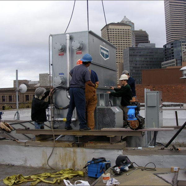 Performance Mechanical Group’s technicians installing a large HVAC unit on a city rooftop.