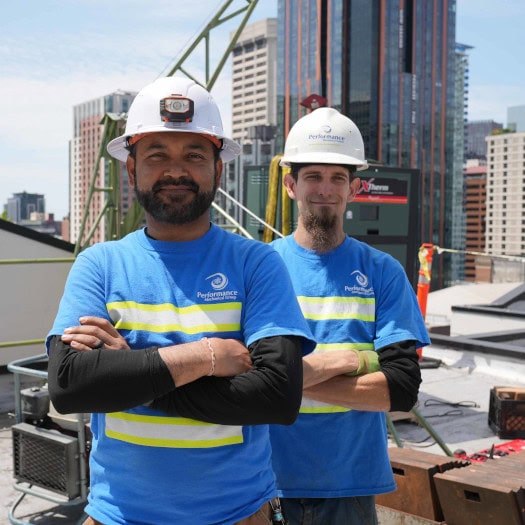 Performance Mechanical Group’s technicians standing at the bottom of a building, watching material get brought up to the rooftop.